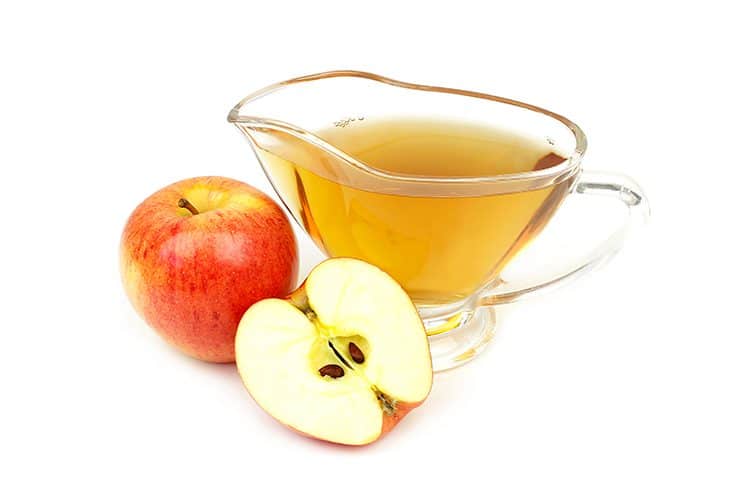 A glass of apple cider vinegar with apples