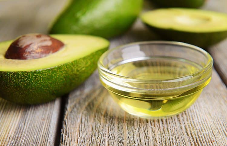 A bowl of avocado oil with an avocado next to it