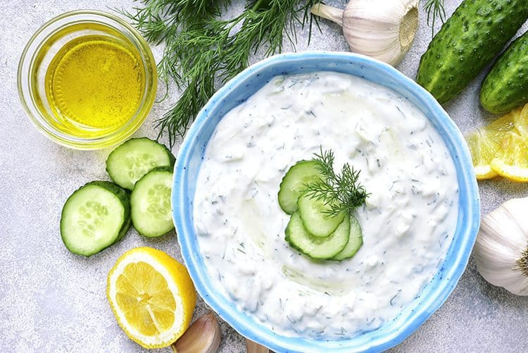 Tzatziki in a blue bowl surrounded by ingredients