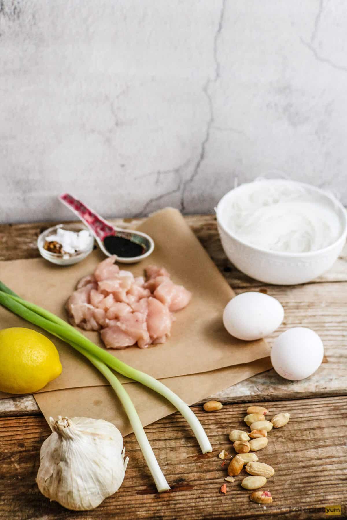 Lemon, garlic, green onion, diced chicken, eggs, peanuts, bowls and a spoon on a table