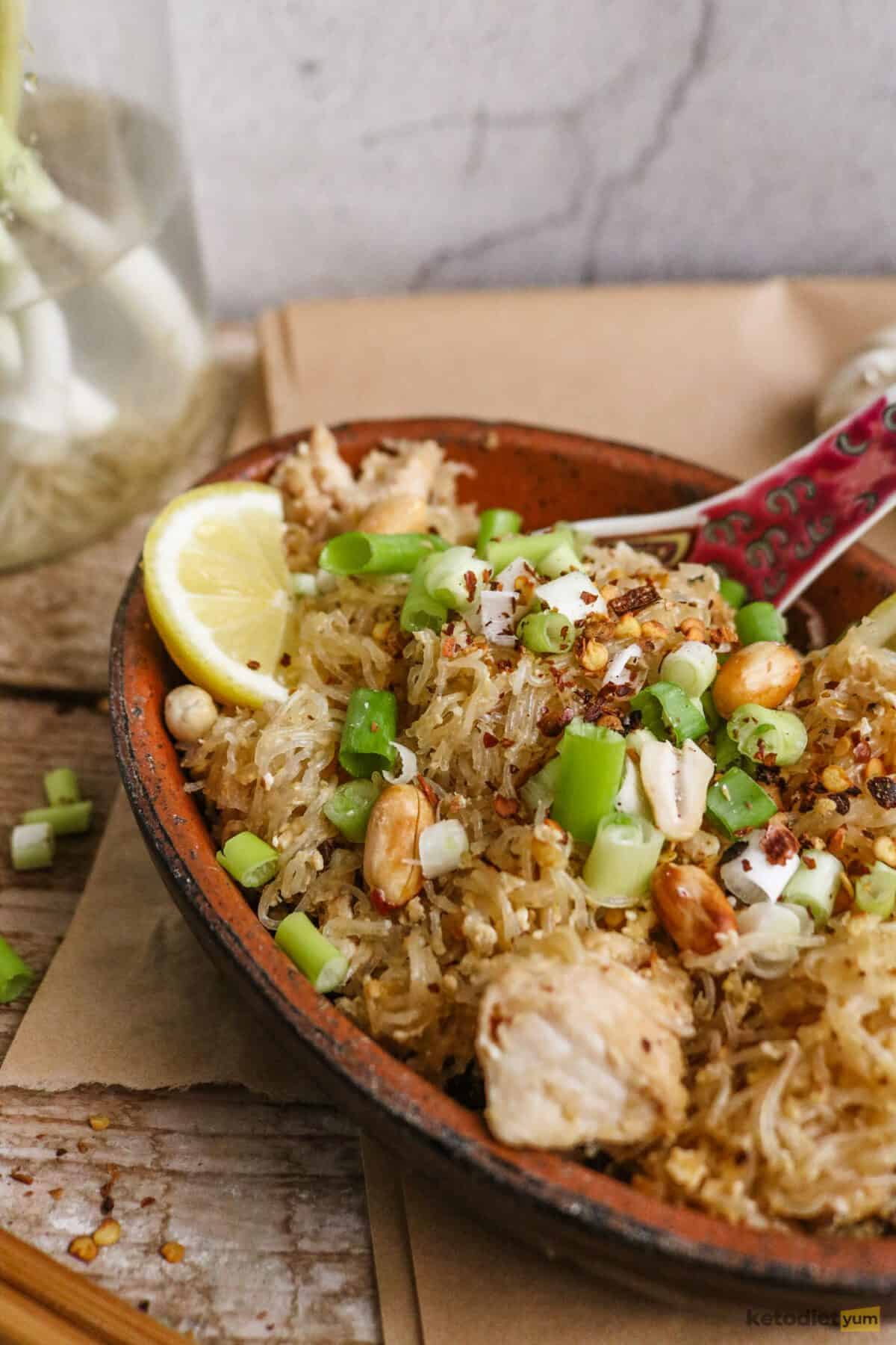 Bowl of keto pad thai garnished with green onions and lemon wedges