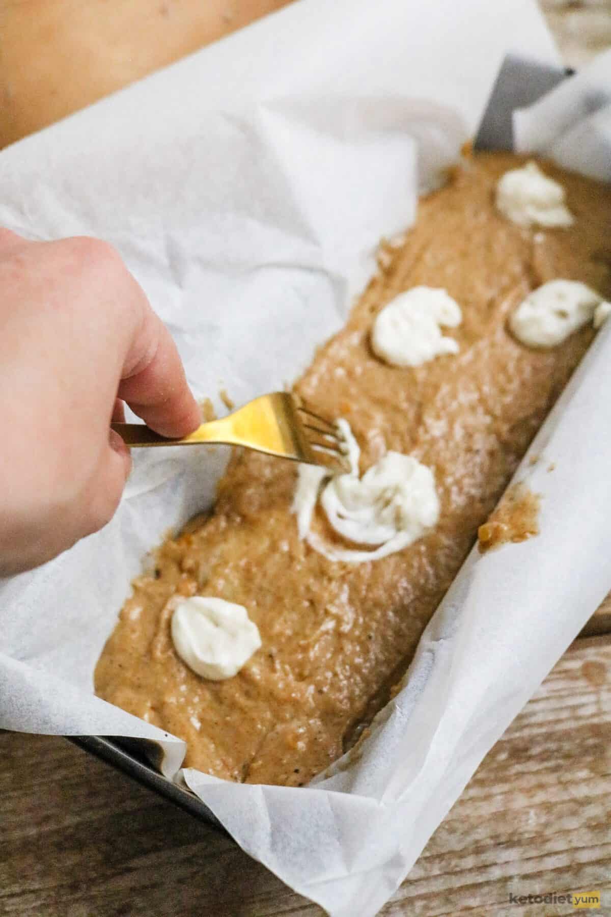 A lined loaf pan filled with keto pumpkin bread batter and topped with a cream cheese filling