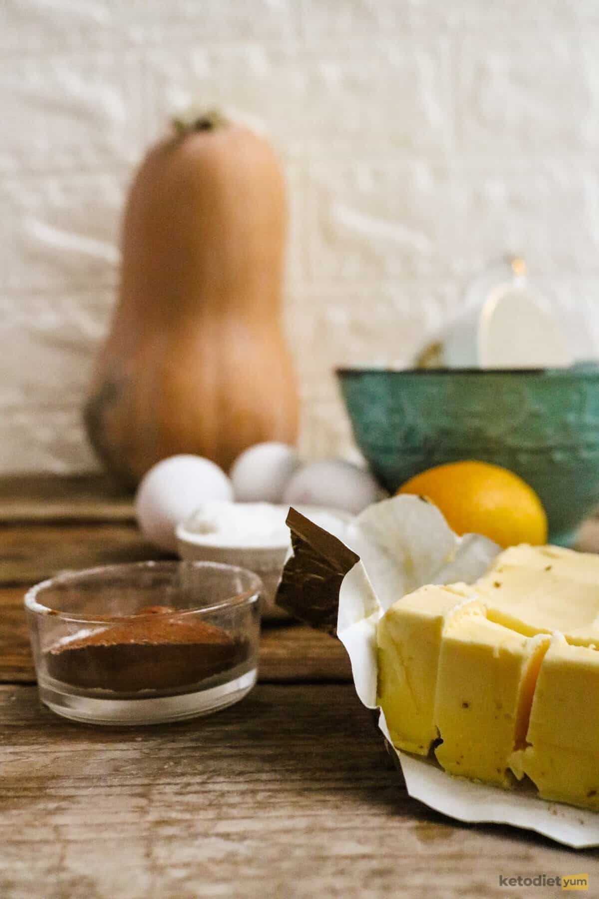 Ingredients arranged on a table to make keto pumpkin bread including pumpkin, butter, eggs, Erythritol, cream cheese, almond flour and spices