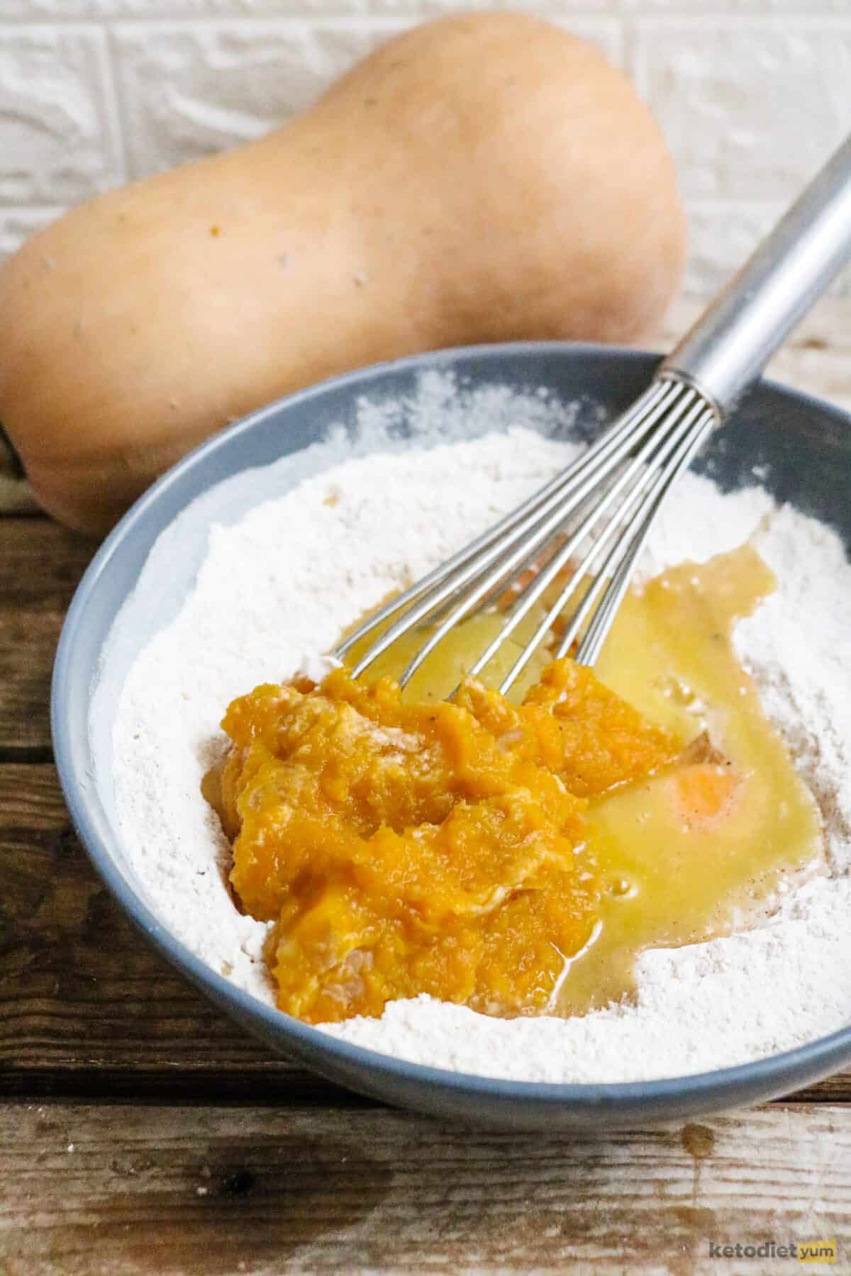 A bowl of dry ingredients having eggs, melted butter and pumpkin puree whisked in