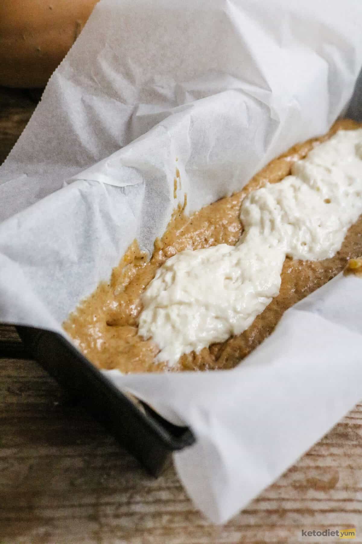 A lined loaf pan filled with keto pumpkin bread batter and topped with a cream cheese filling