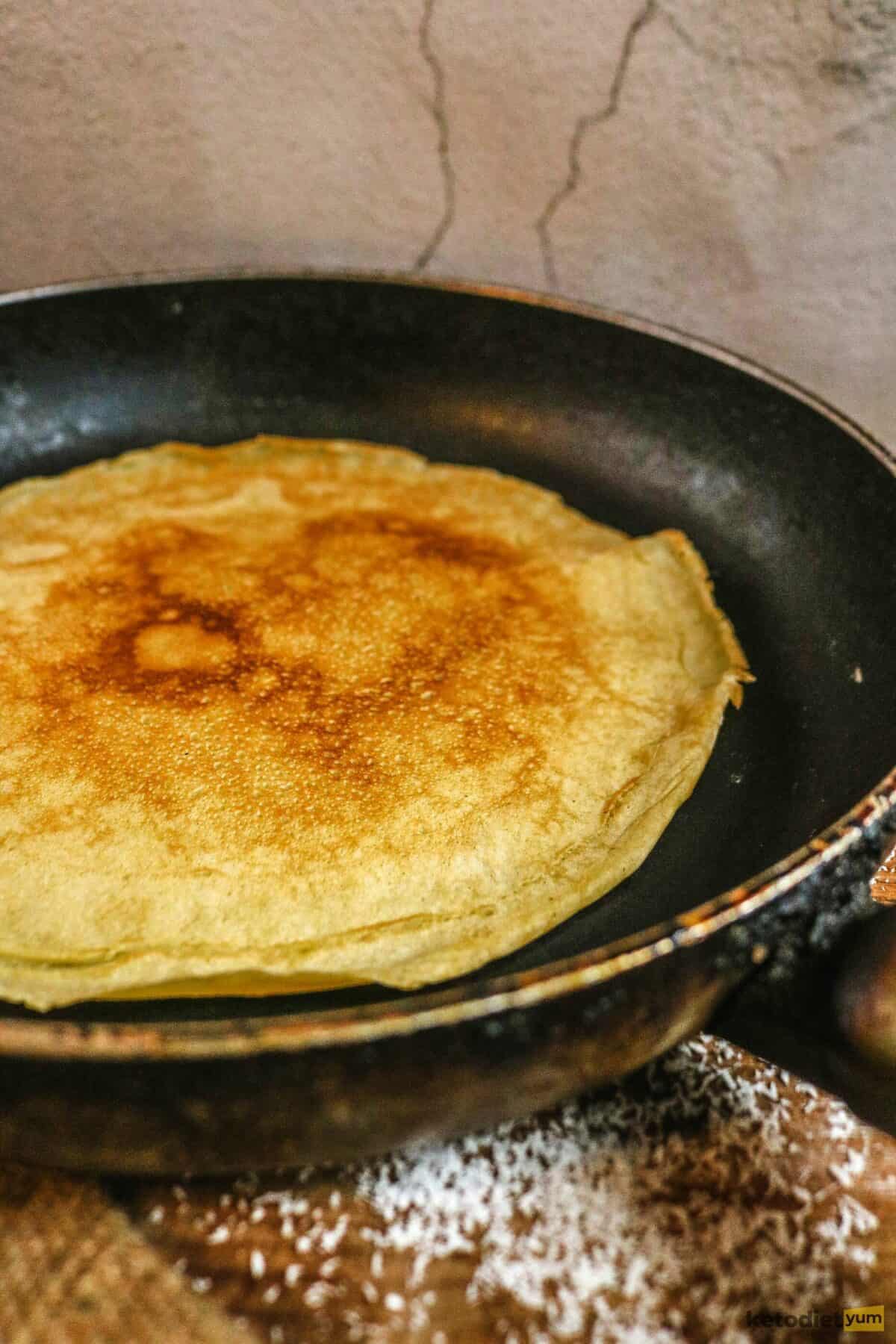 Coconut flour crepes cooking in a greased pan