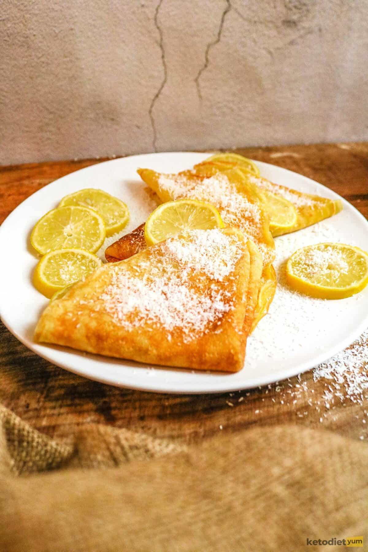 Keto Coconut Flour Crepes Gluten free crepes on a white plate with lemon and coconut flakes