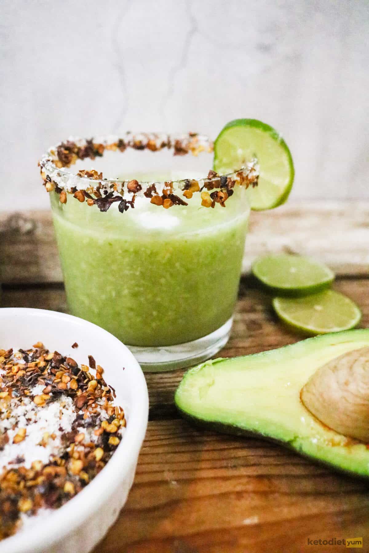 Avo keto margarita with chili salt rim and lime slice garnish with half avocado and bowl of chili salt in the foreground