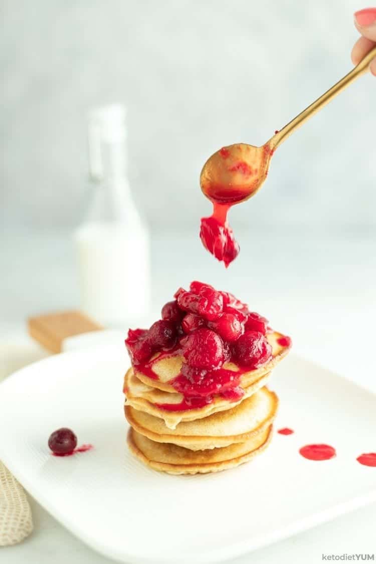 Cranberry Keto Pancakes Recipe A stack of keto pancakes being drizzled with hot home made cranberry sauce.