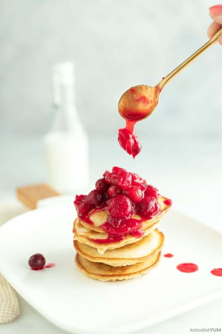 A stack of keto pancakes being drizzled with hot home made cranberry sauce.