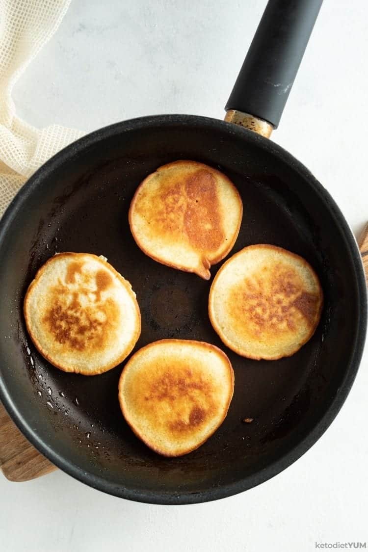 Golden brown keto pancakes cooked to perfection in a pan and ready to serve with cranberry sauce.