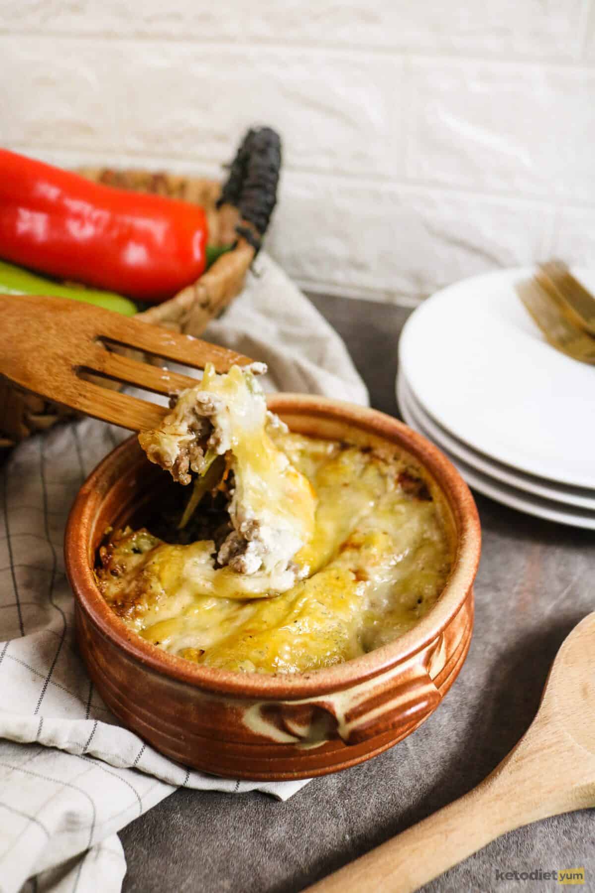 Brown casserole dish with a wooden spoon pulling a serving of cheesy casserole out