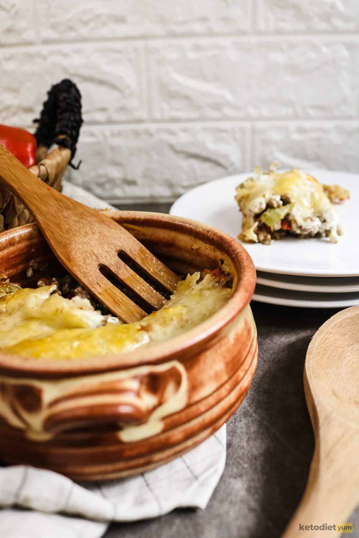 Casserole in a baking dish with a wooden spoon and plates with a serving of casserole in the background