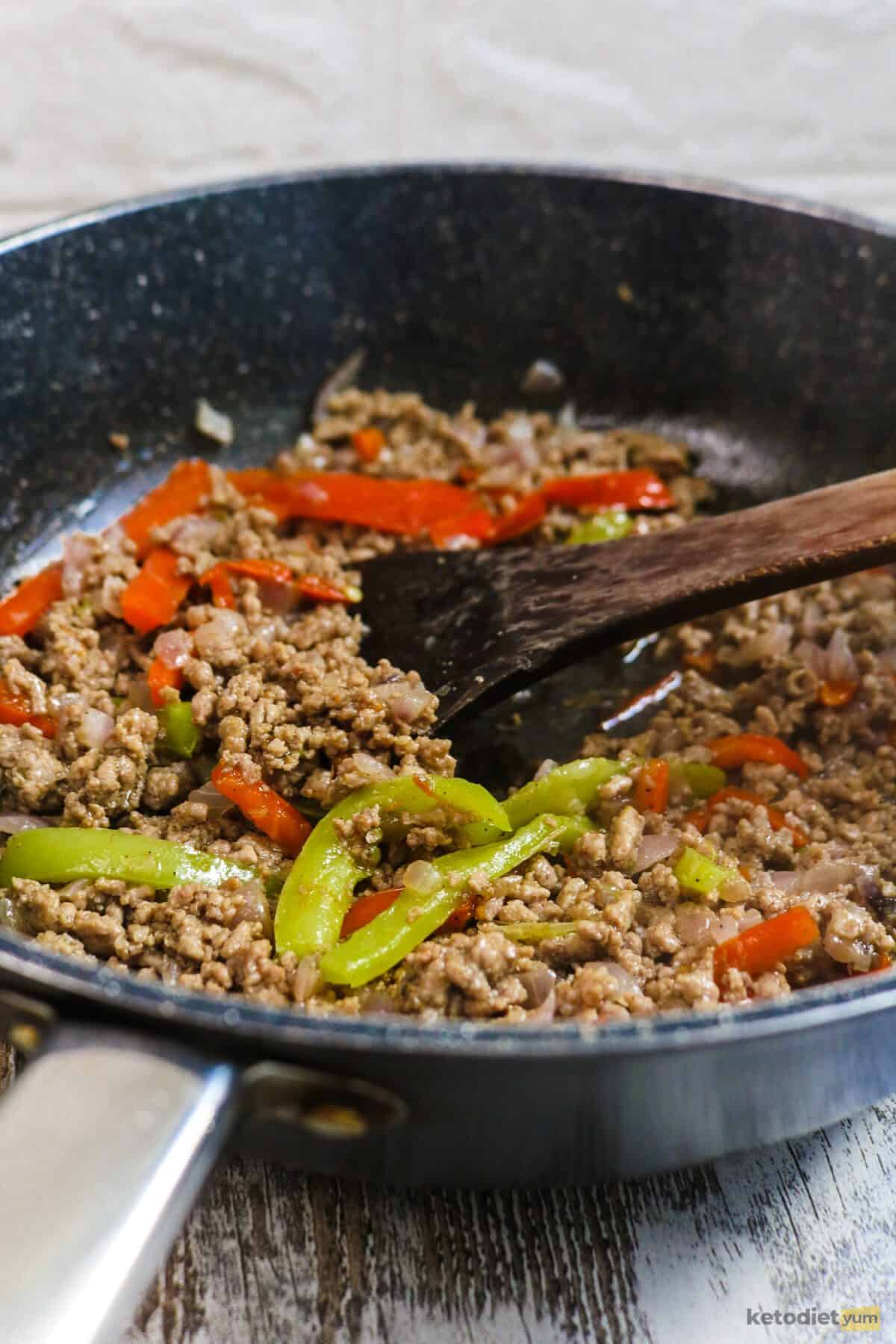 Black frying pan with ground beef, red peppers, green peppers and a wooden spoon