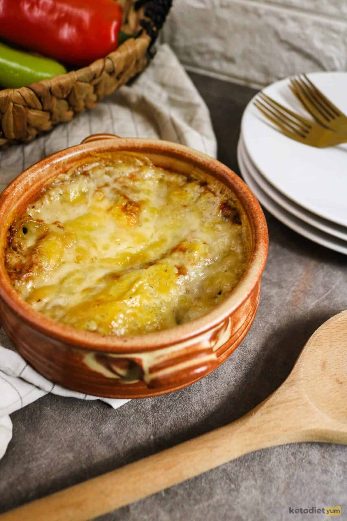 Brown casserole dish on a table with a golden cheese layer on top and plates in the background and a wooden spoon in the foreground