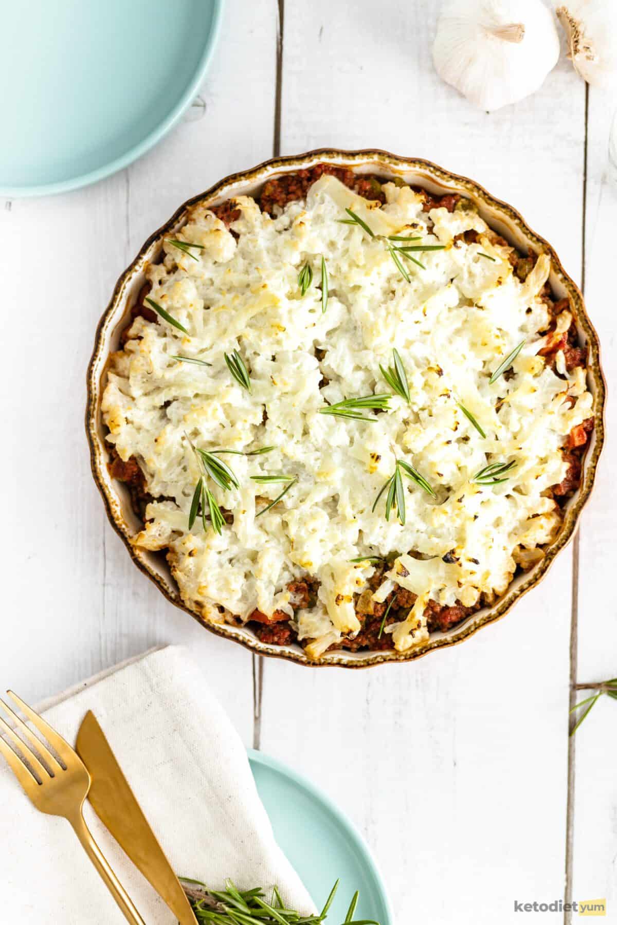 Baking dish topped with golden cauliflower and rosemary sitting on a table with utensils in the background