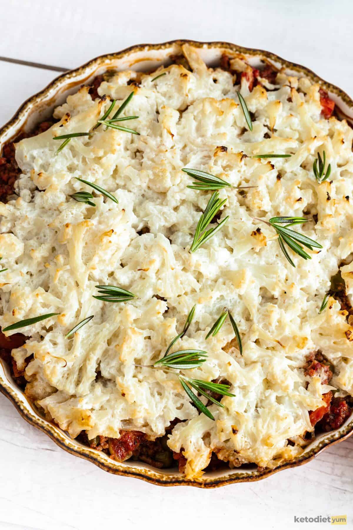 Baking dish with a shepherd's pie that has a golden cauliflower topping and rosemary sprinkled on top