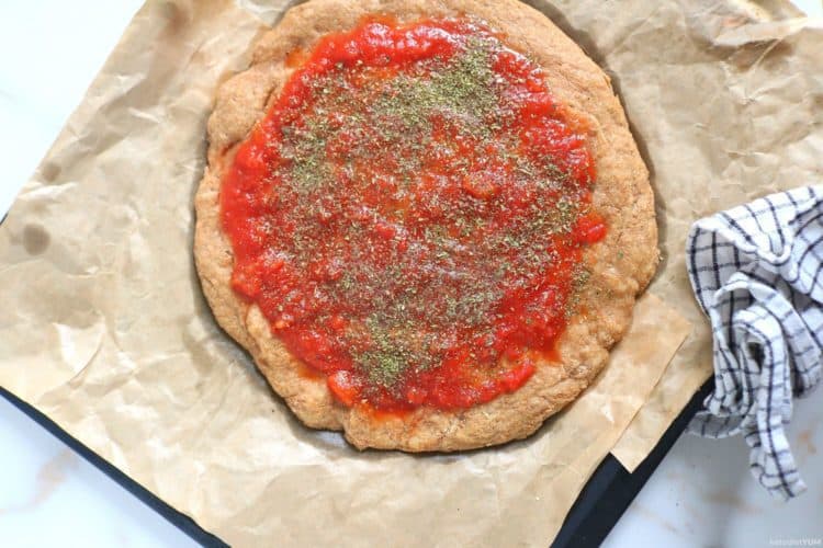 Topping the almond flour pizza crust with crushed tomatoes and seasonings