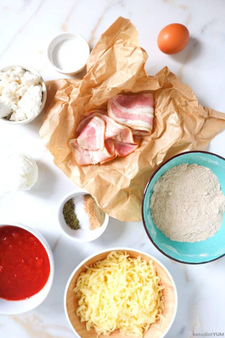 Ingredients needed to make a low carb almond flour pizza crust topped with bacon and feta