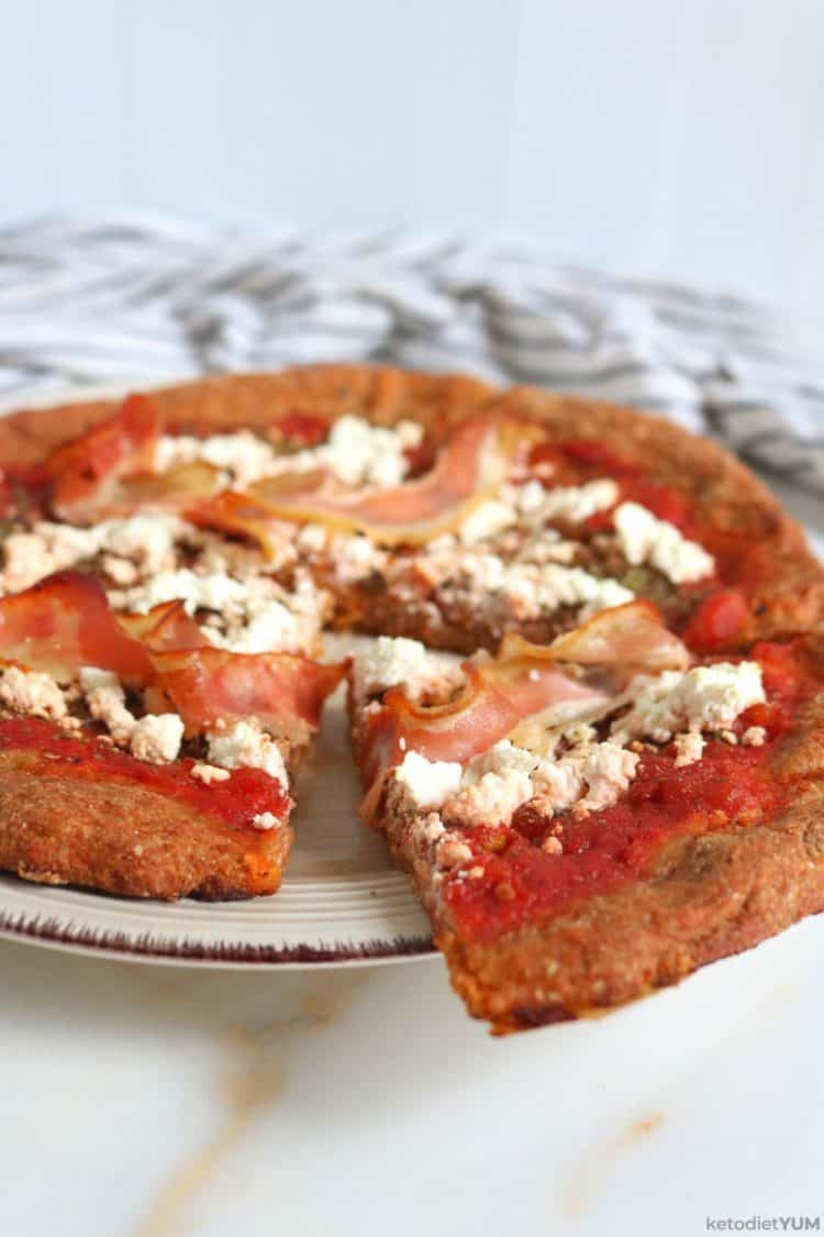 Delicious keto almond flour pizza crust topped with crushed tomatoes, feta cheese and bacon