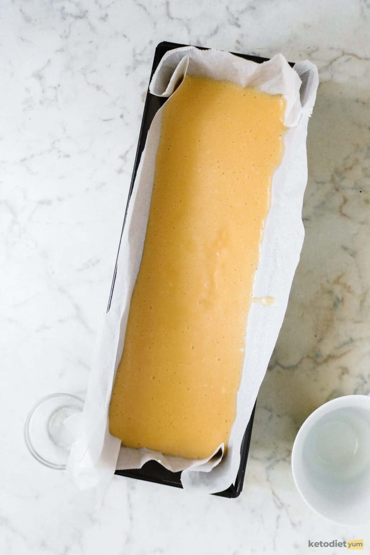 Lined loaf pan filled with egg loaf batter on a white table