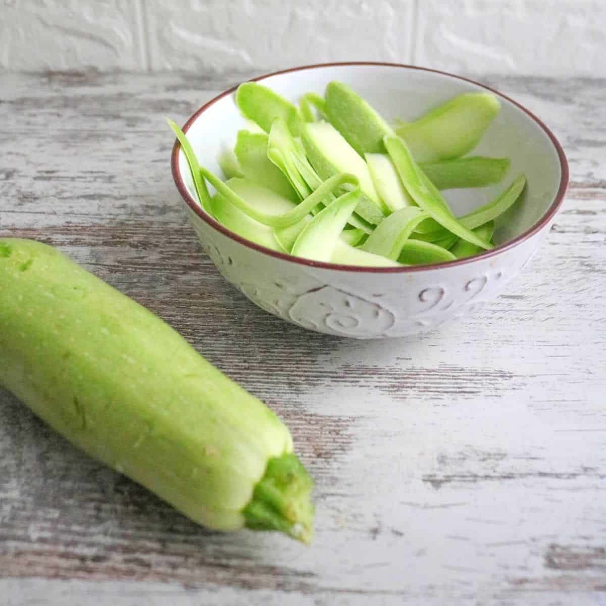 Bowl of sliced zucchini and a whole zucchini