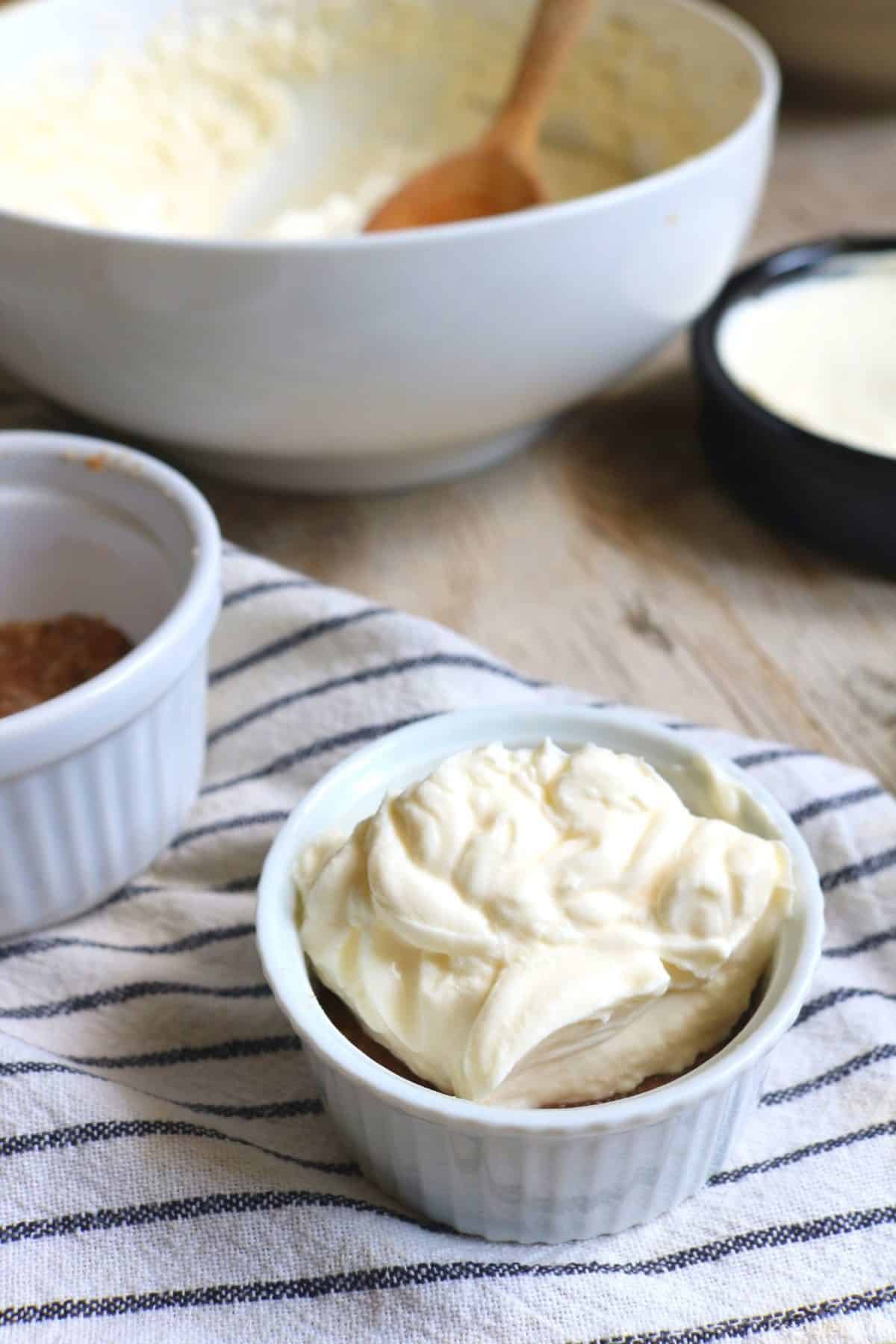 Adding the cream cheese filling mixture into the ramekins filled with the cheesecake base