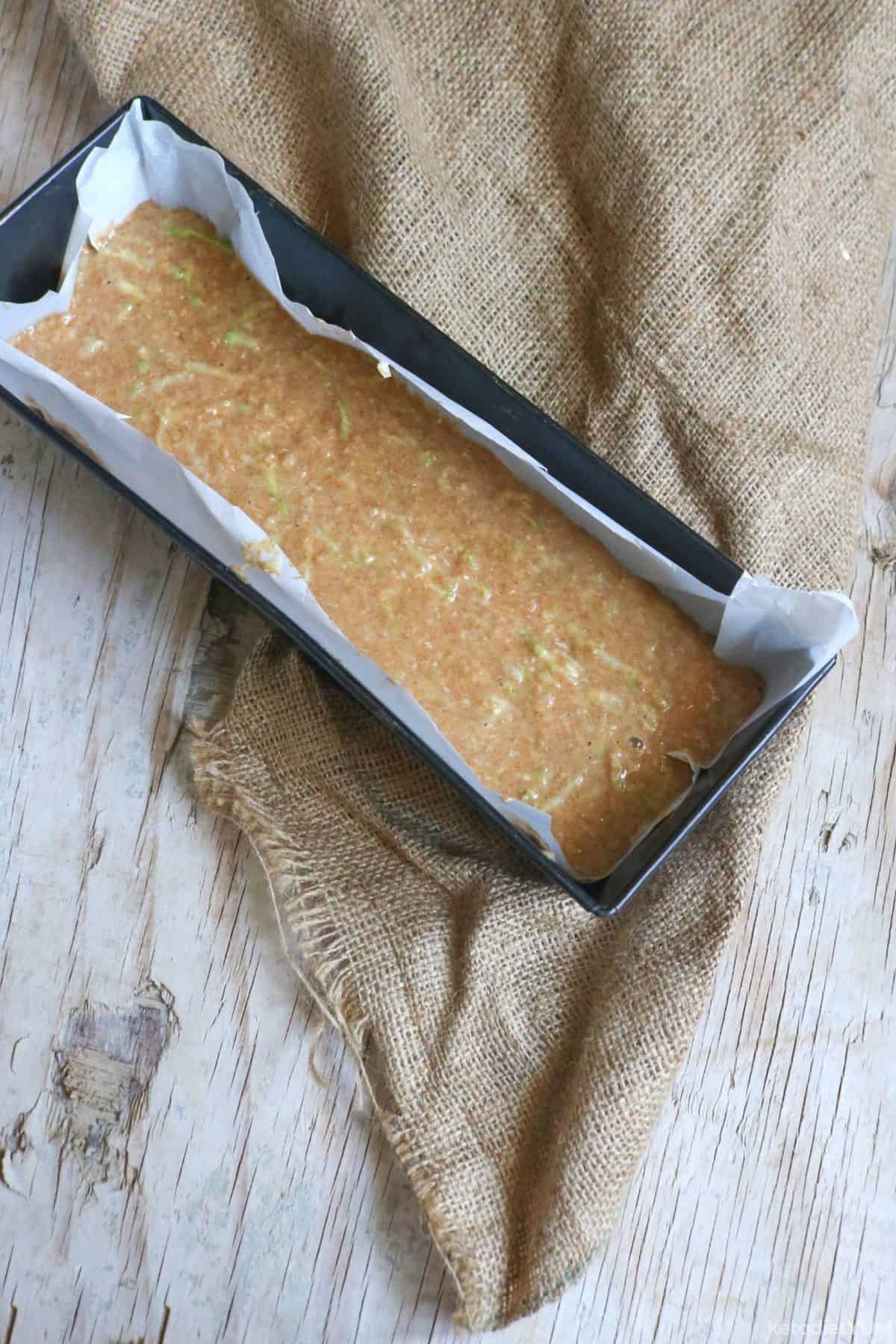 Zucchini bread batter poured into a lined loaf pan and ready to bake