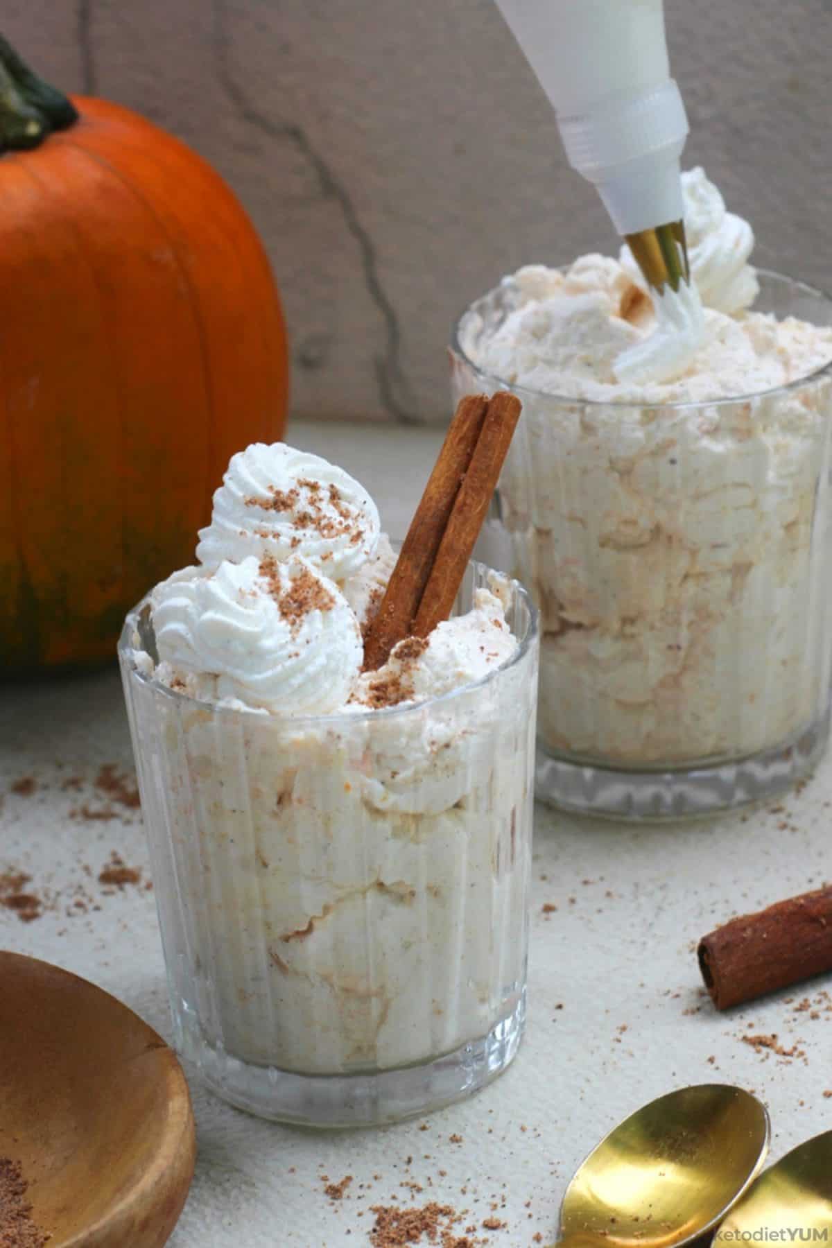 Delicious keto pumpkin mousse served with a sprinkle of pumpkin pie spice and a stick of cinnamon for decoration