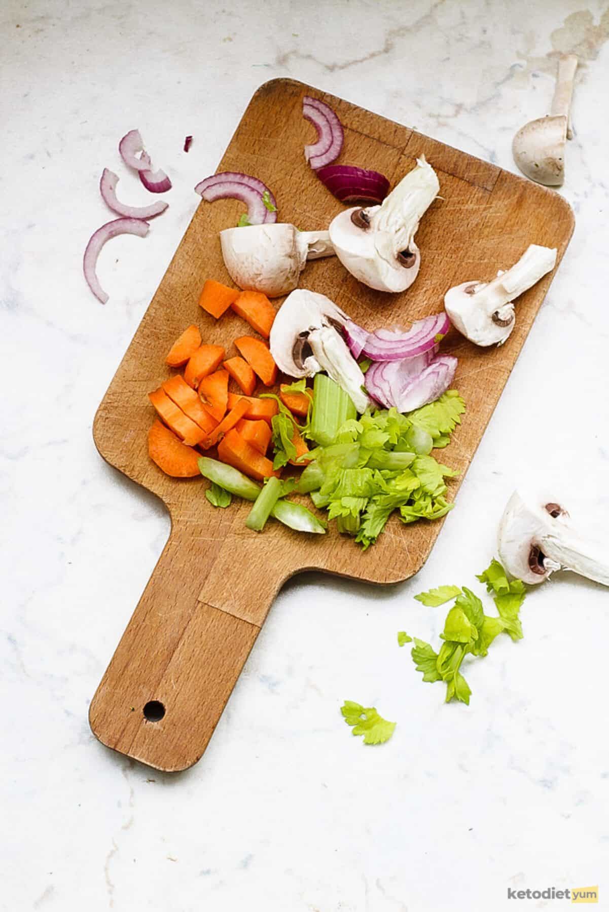 Chopped button mushrooms, red onion, carrot and celery on a chopping board