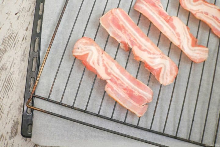 Placing bacon strips on an oven rack to bake in the oven