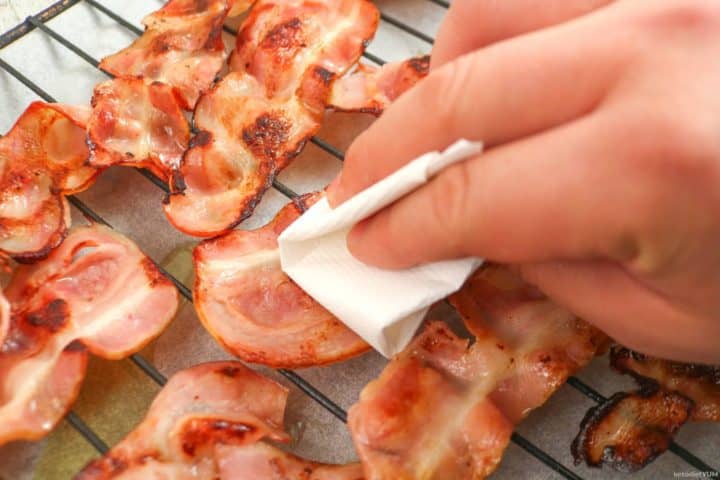 Patting excess grease off the crispy bacon with a paper towel