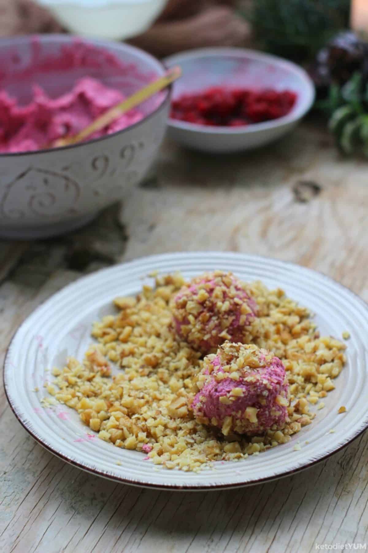 Rolling raspberry cheesecake bites in chopped walnuts on a white plate