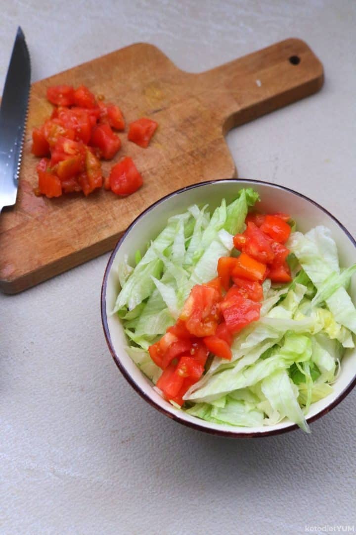 Adding chopped romaine lettuce and chopped tomato to a bowl