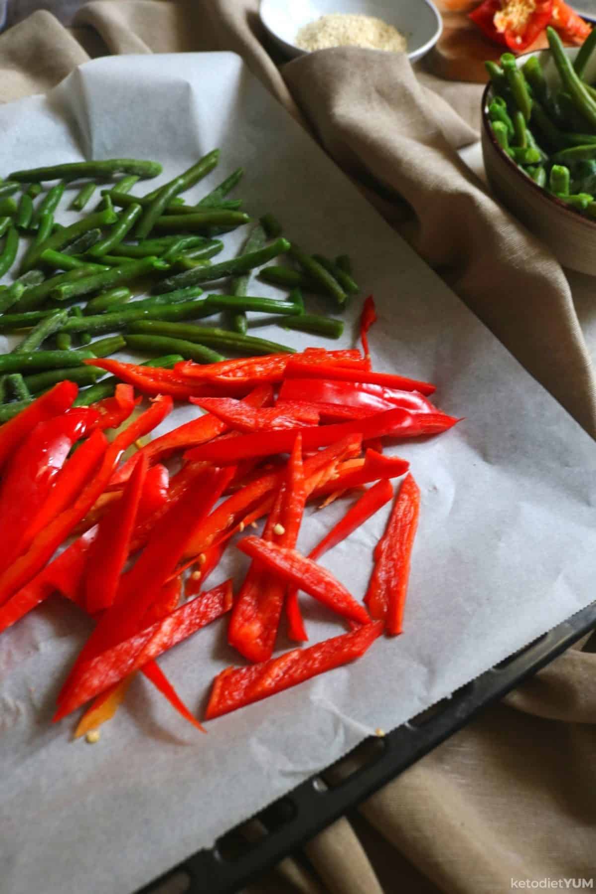 Placing the sliced red pepper and green beans on the baking tray ready to bake