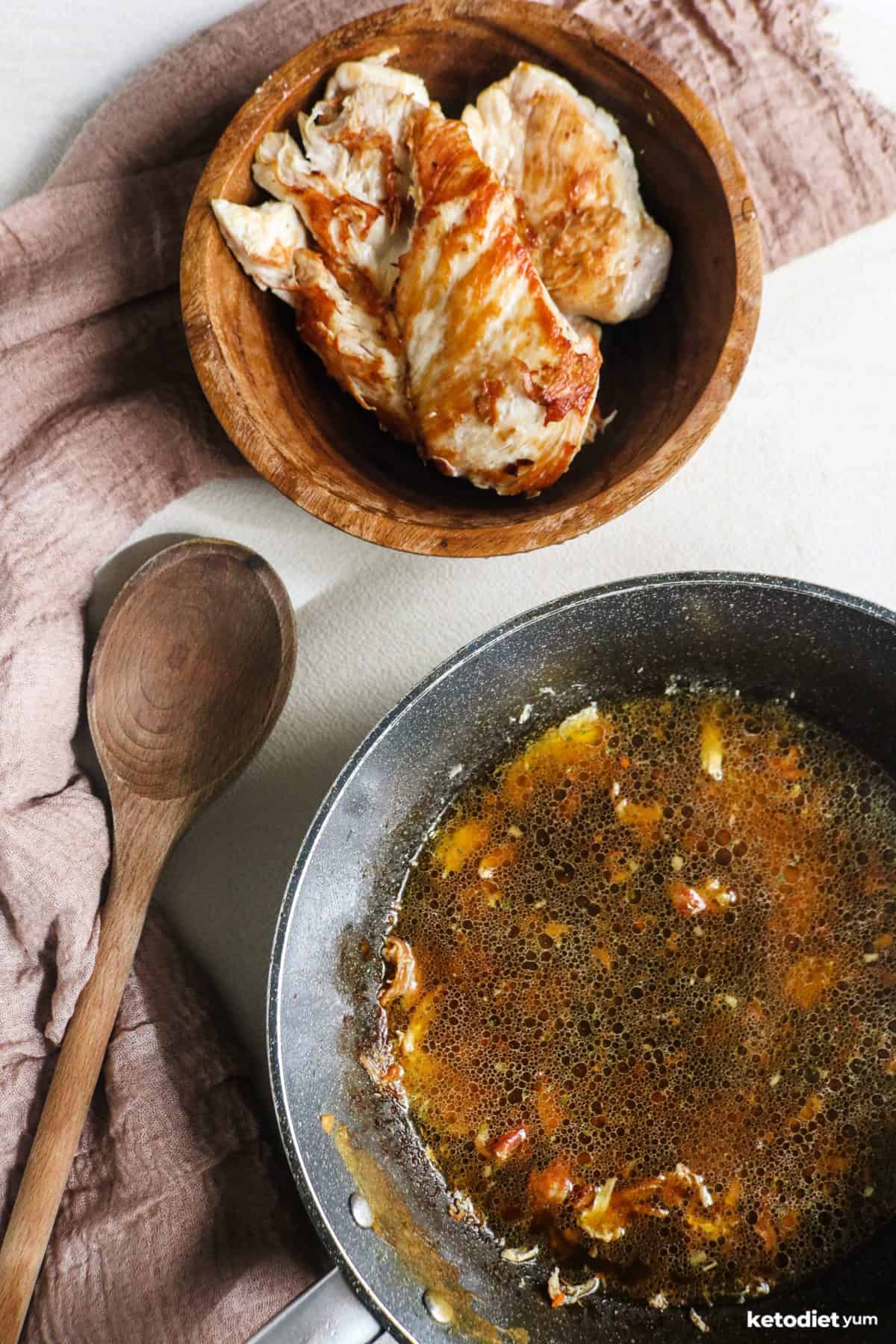 Golden chicken breasts in a bowl with a pan being deglazed with chicken broth