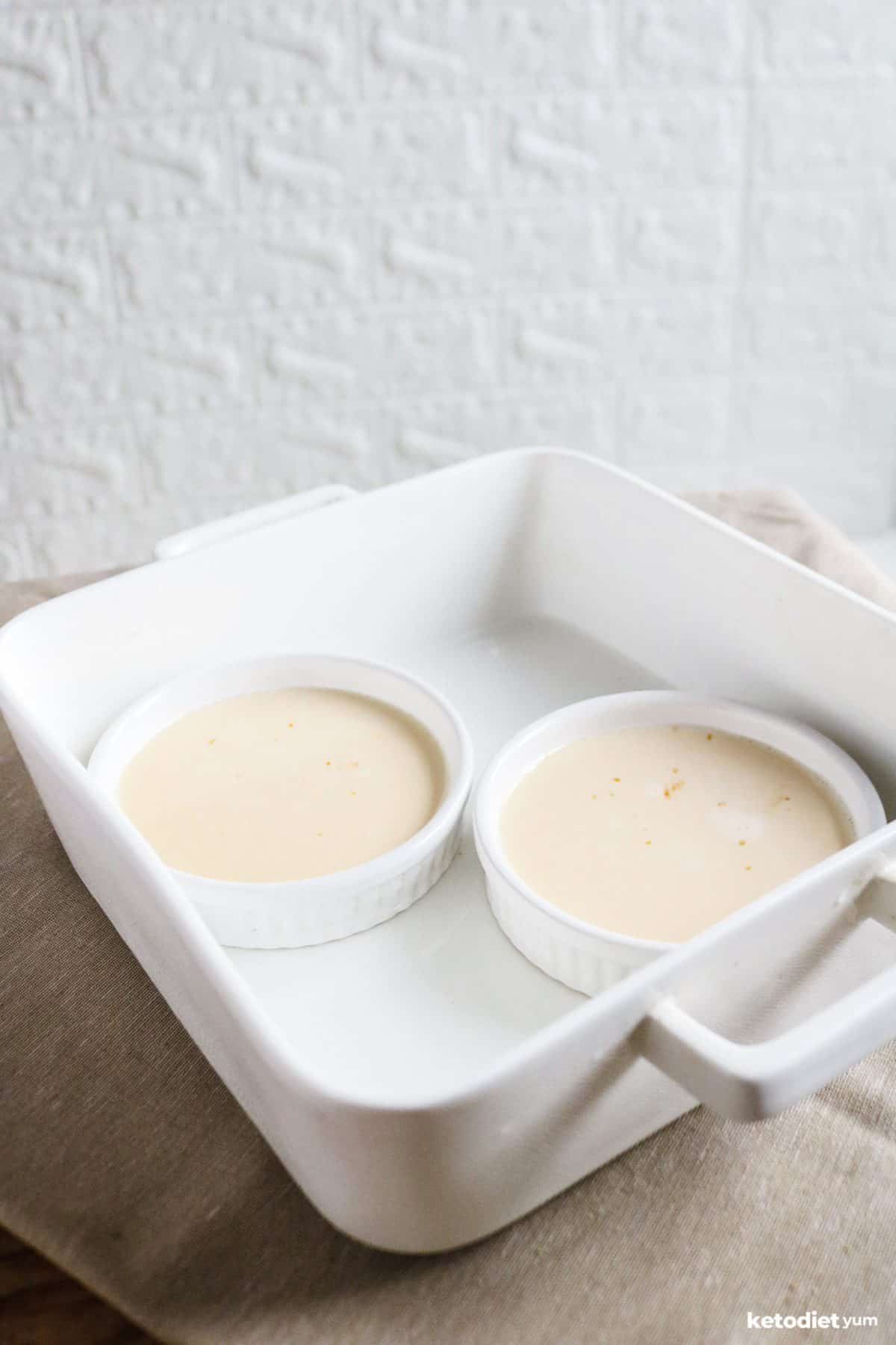 Two ramekins filled with low carb custard mixture in a baking dish ready to bake