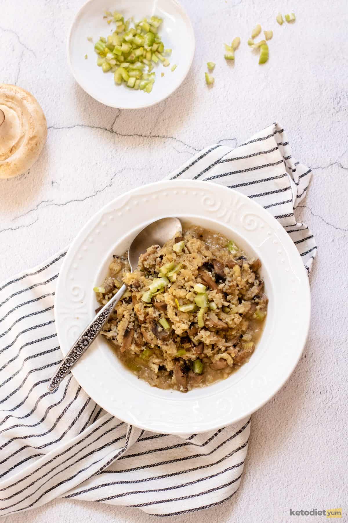 A low carb keto cauliflower mushroom risotto served on a white plate and topped with diced celery