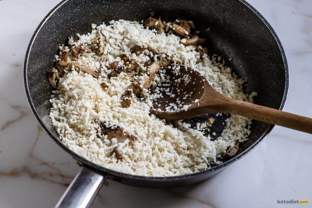 Adding cauliflower rice to a pan of sautéed mushrooms and celery