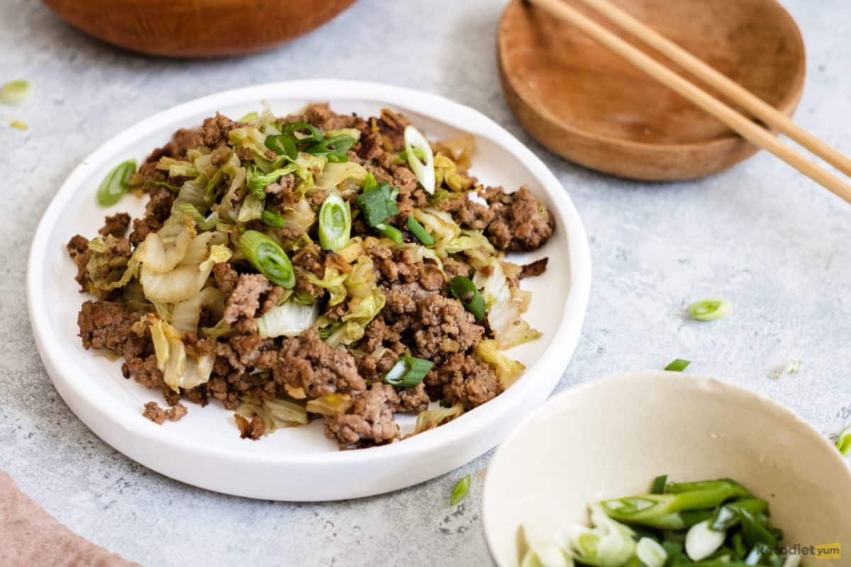 Cabbage stir fry with ground beef served on a white plate and garnished with fresh scallions