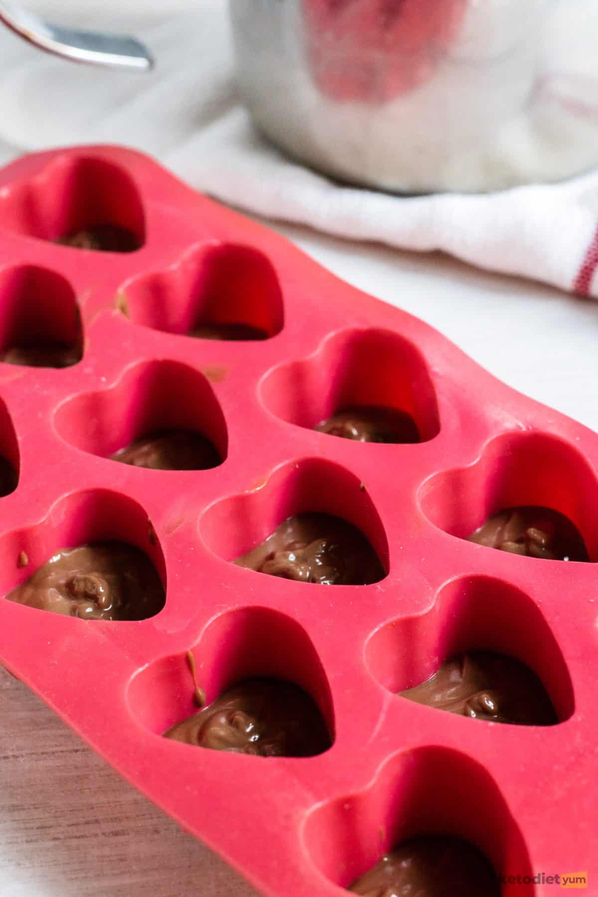 Filling a heart-shaped silicone tray with melted dark chocolate and coconut oil
