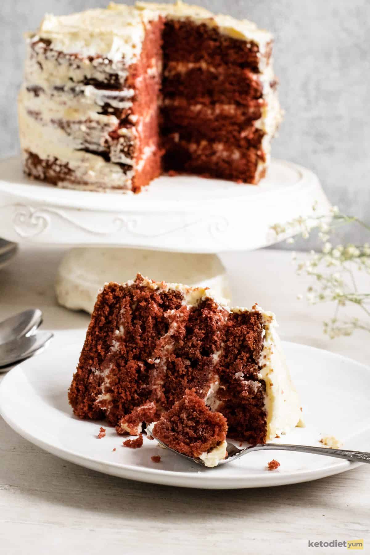 A slice of sugar free red velvet cake on a white plate with a spoon