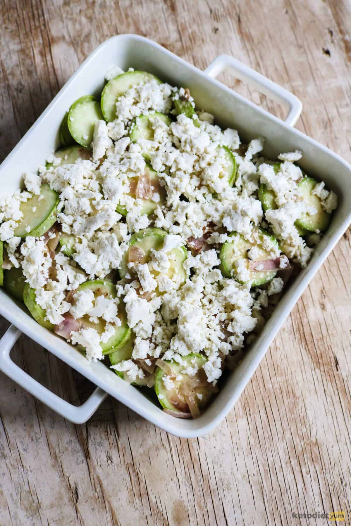 A feta, mozzarella, red onion, sour cream and garlic sauce poured over sliced zucchini ready to bake