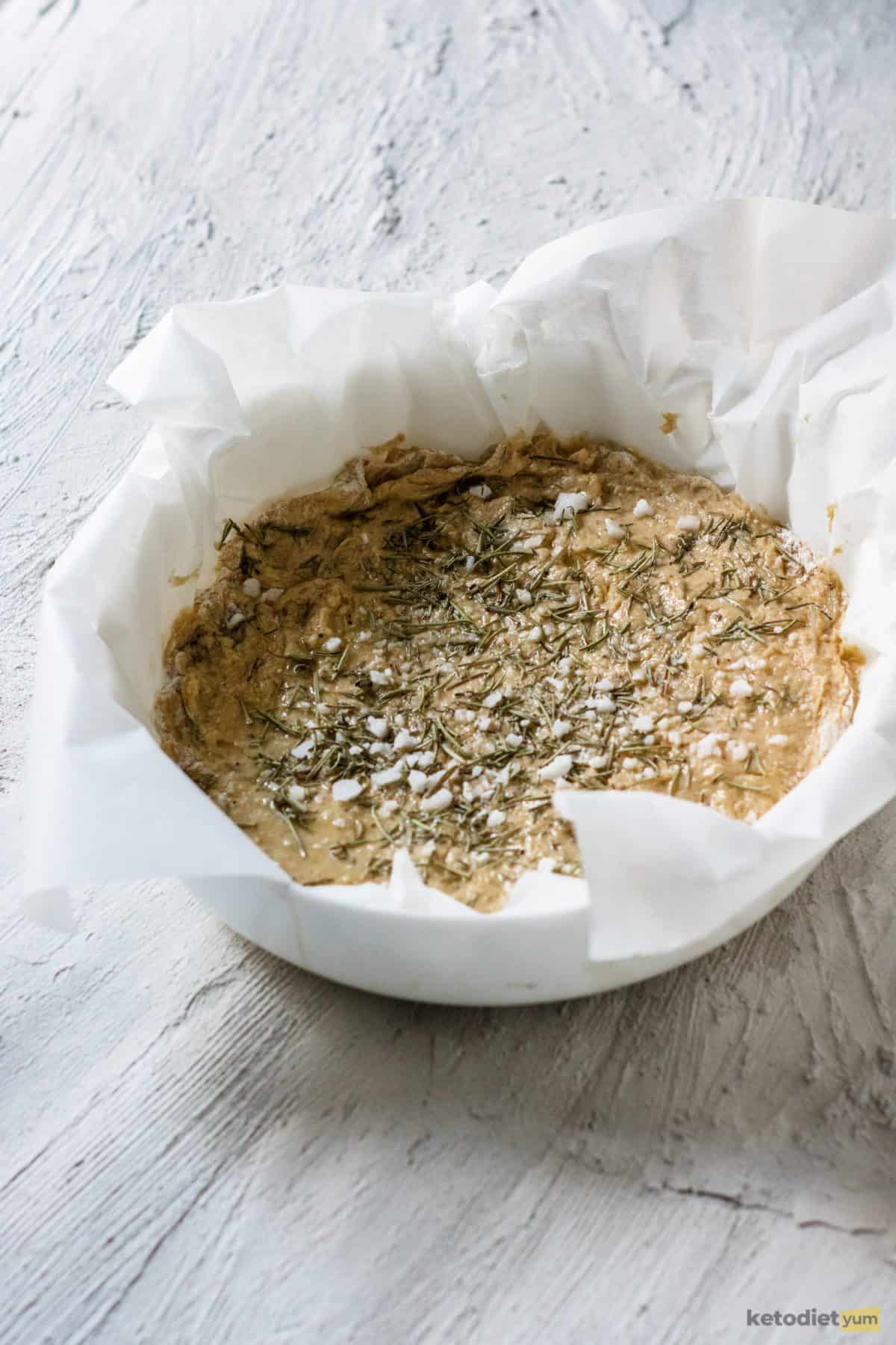 Rosemary focaccia dough in a baking pan topped with rosemary and sea salt flakes and ready to bake