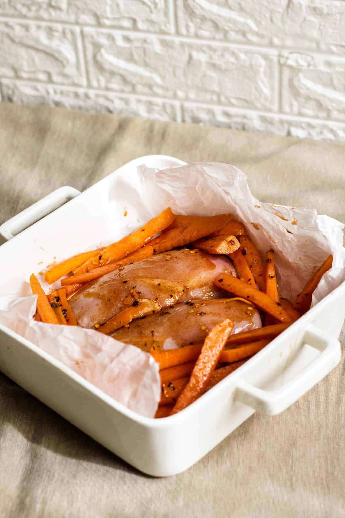 Chicken breasts and sliced carrots coated in a spicy sauce and placed in a lined baking dish ready to bake