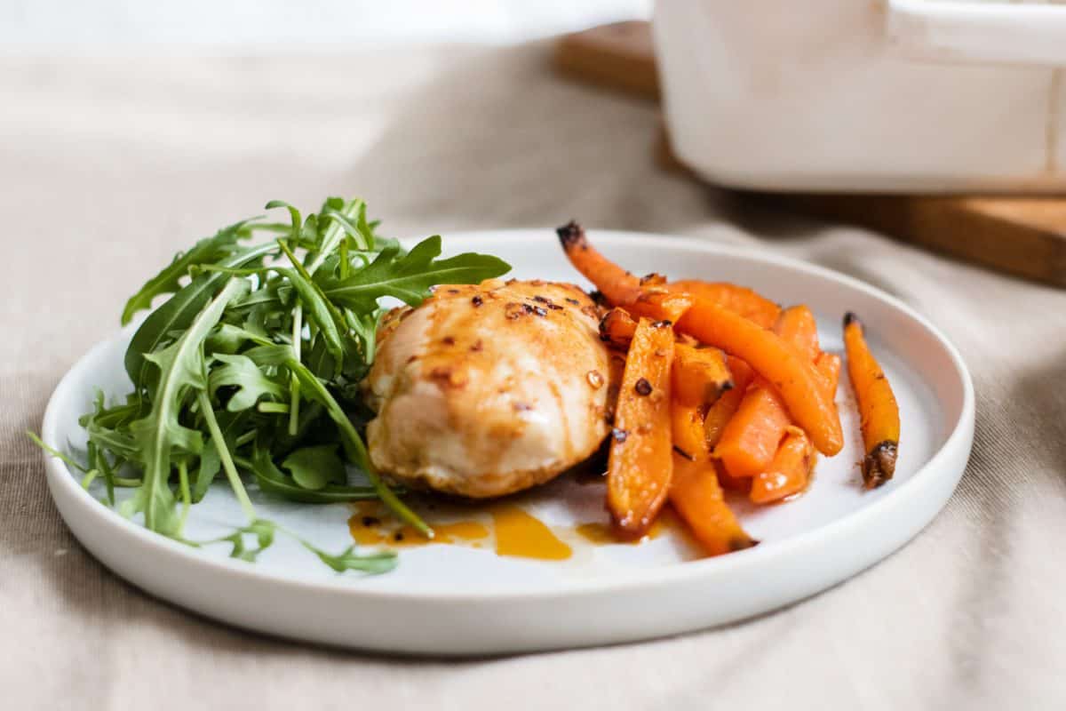 Roasted chicken and vegetables (carrots) and a side salad on a white plate