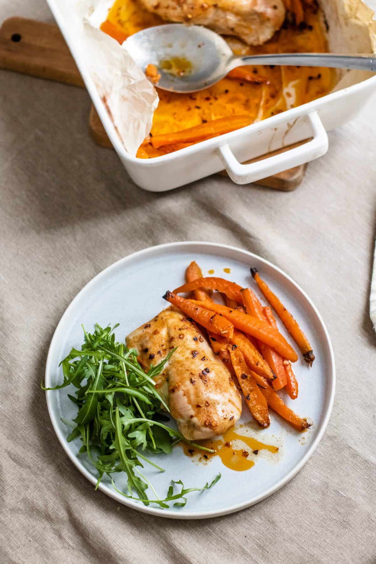 Spicy roasted chicken and carrots with a green salad on a white plate