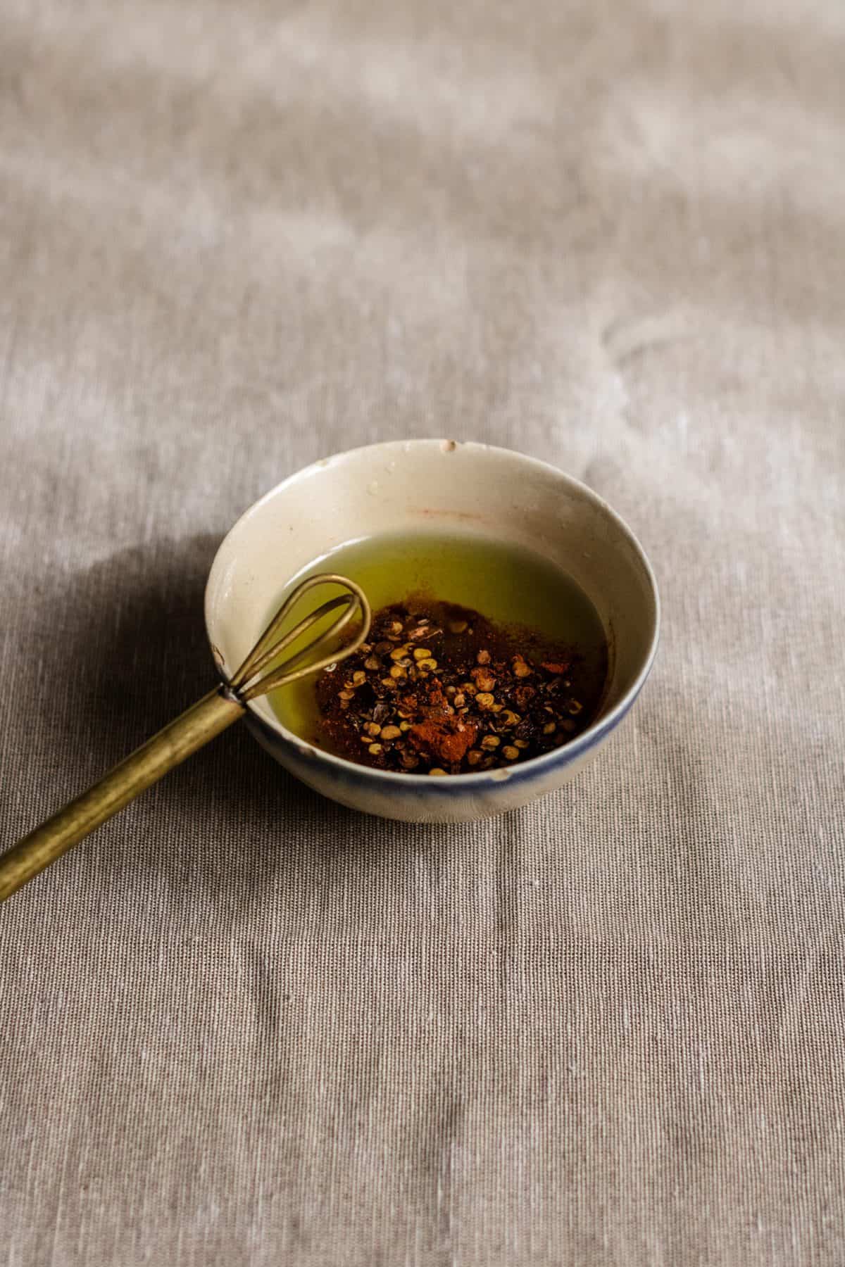 A mixing bowl with olive oil, garlic powder, chili flakes, paprika and salt