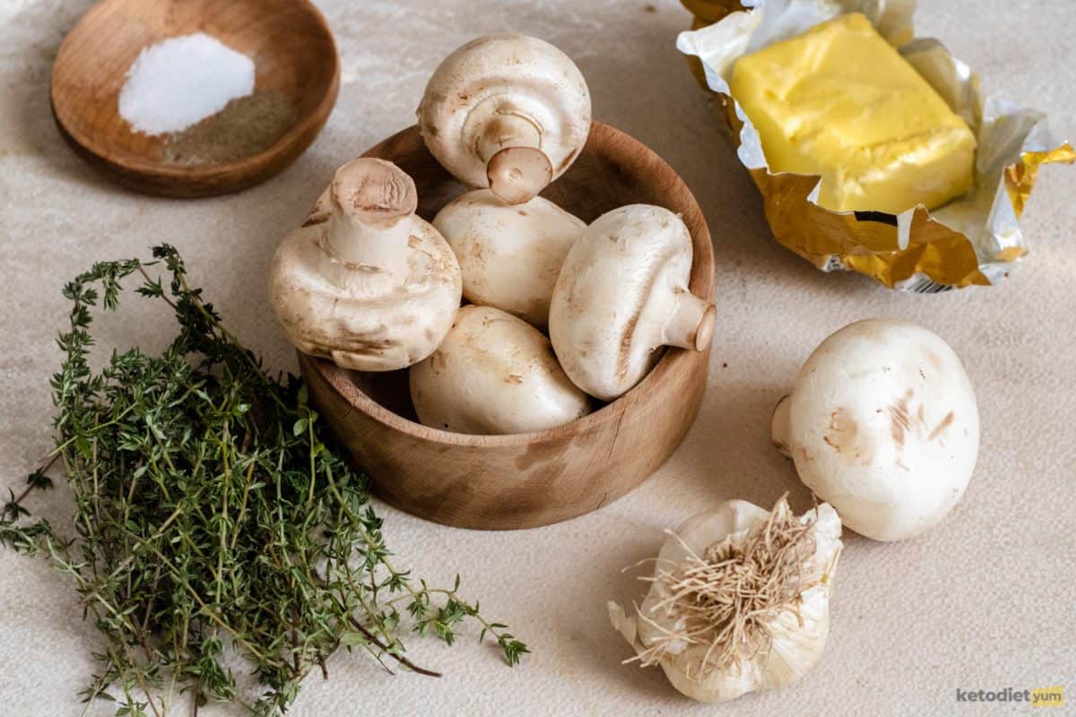 Fresh ingredients on a table including button mushrooms, thyme, butter, garlic, salt and pepper