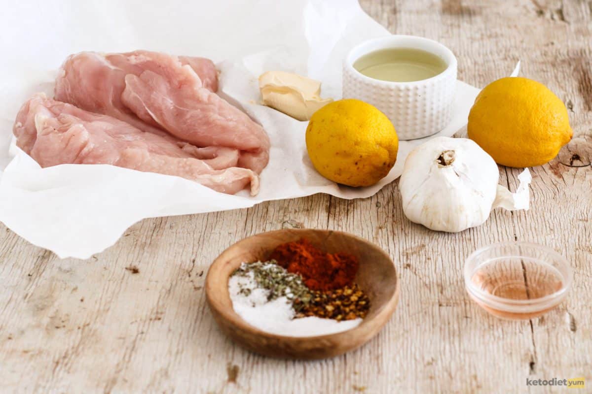 Ingredients arranged on a table including chicken breasts, garlic, lemons, avocado oil, herbs and spices